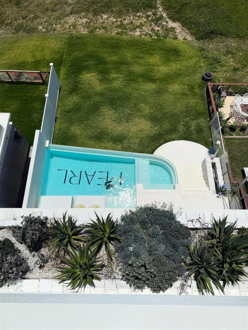 Drone view of a white rendered home and its curved pool